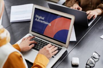 Two professionals work on laptops focusing on digital advertising in an office setting.