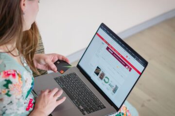 Woman in floral dress shopping online with a laptop and credit card indoors.